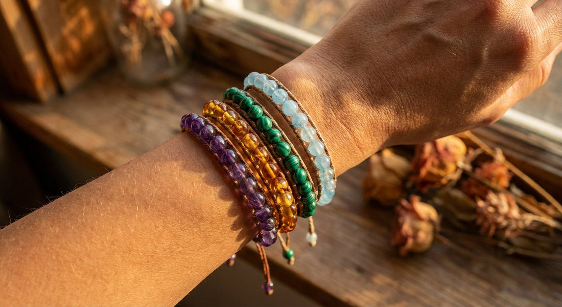 A woman's wrist layered with a stack of colorful handcrafted gemstone bracelets in violet, amber, green, and blue, glowing in warm golden-hour light against a soft earthy background.