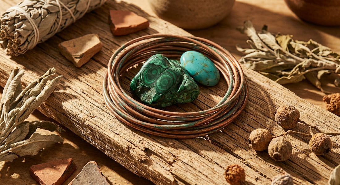 Raw copper wire wrapped around malachite and turquoise stones resting on aged wood with dried botanicals in warm, golden natural light.