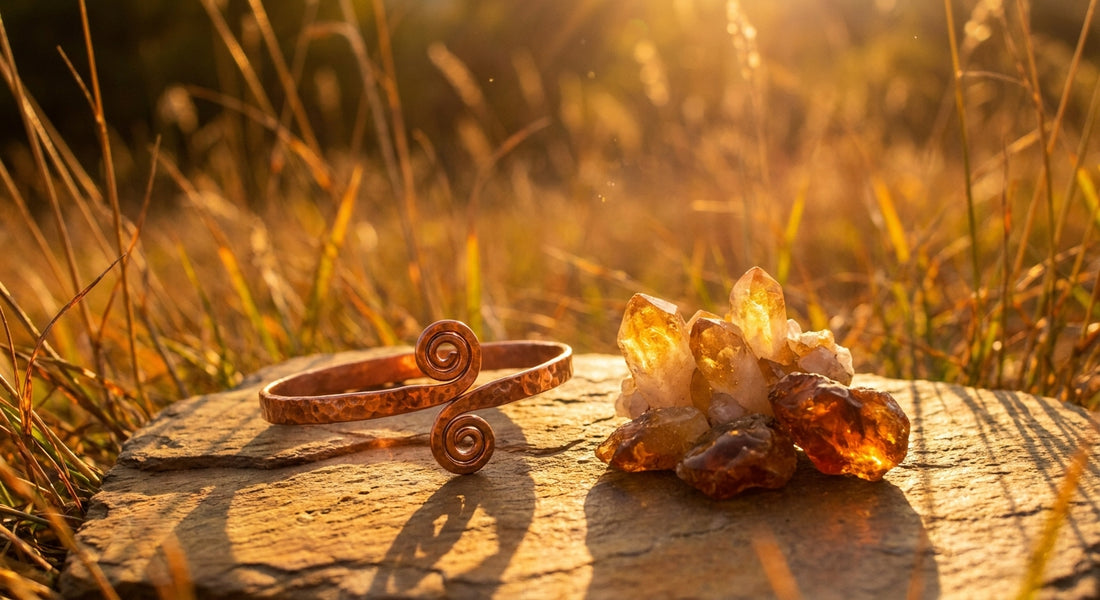 A handcrafted copper cuff bracelet resting on a sun-warmed stone surrounded by golden citrine and amber crystals, bathed in warm late-summer sunlight with wild grasses blurred in the background.