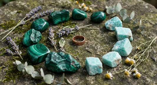 Raw malachite and amazonite crystals arranged with dried botanicals and a handcrafted copper ring on a weathered stone surface in soft natural light.
