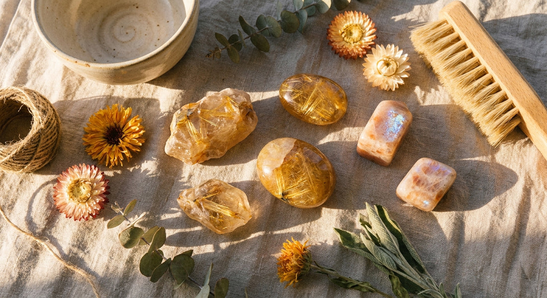 Golden rutilated quartz and sunstone crystals arranged on linen with dried botanicals, bathed in warm morning sunlight.
