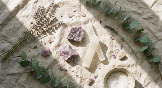 Raw lepidolite and selenite crystals arranged on linen cloth with dried lavender and eucalyptus in soft morning light.