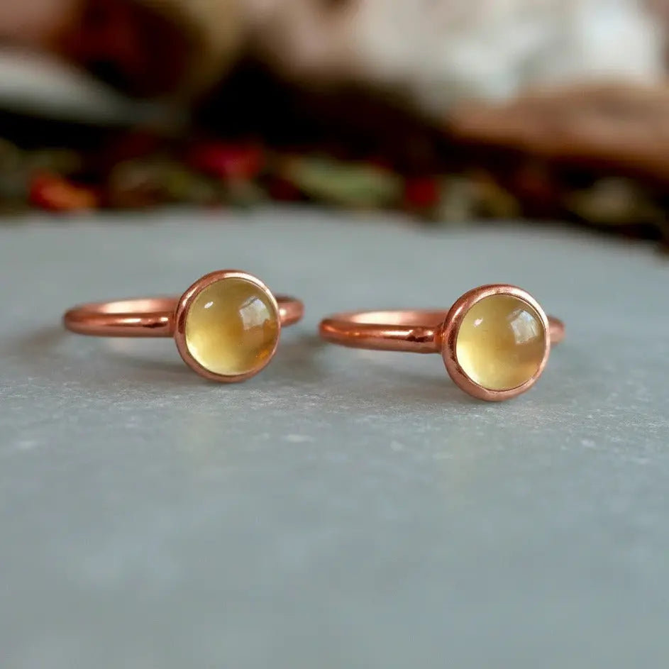 May include: Two copper rings with yellow gemstones. The rings are simple and delicate, with a smooth, rounded band and a small, round gemstone set in the center.