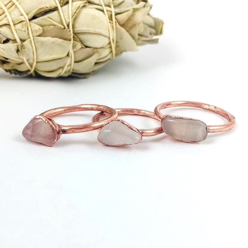 Three rose quartz copper rings styled on white background, showing soft pink stone tones