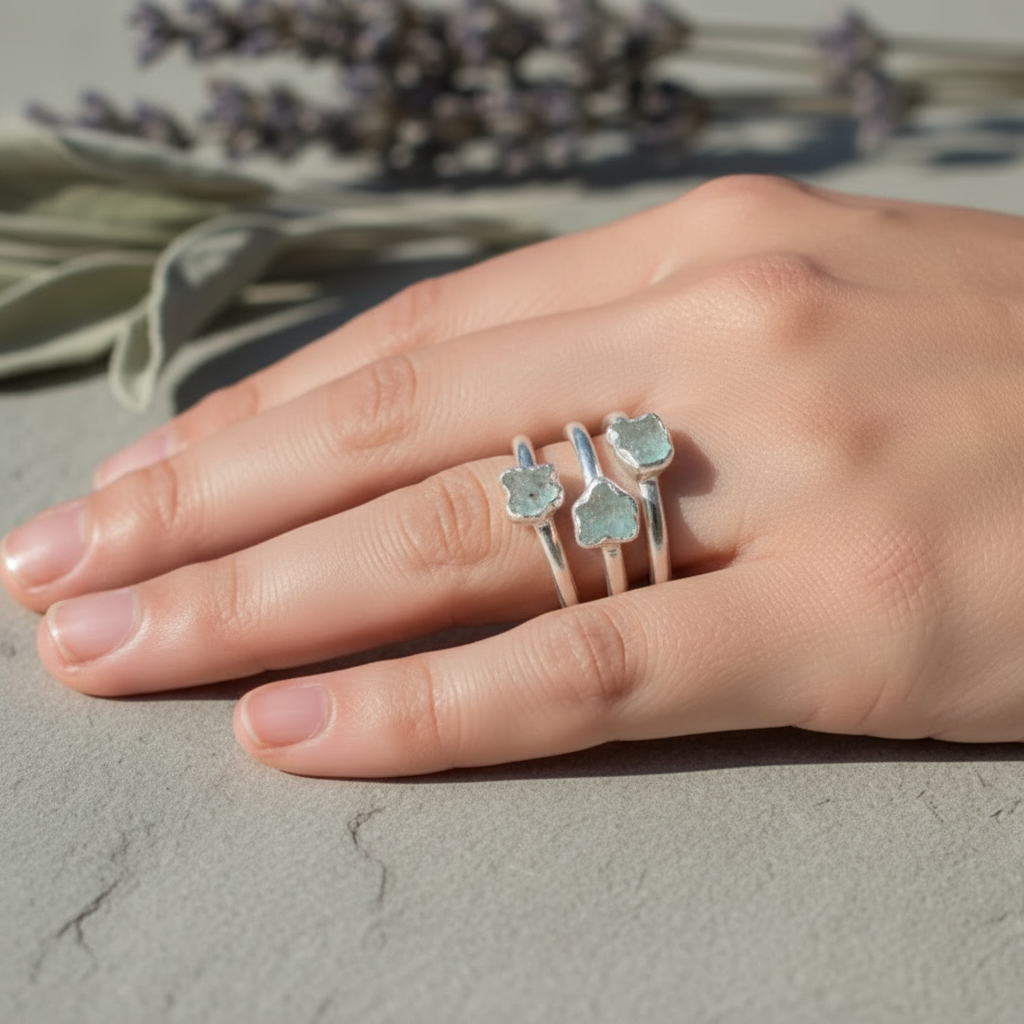 Three dainty raw aquamarine silver stacking rings worn across fingers on hand with dried botanicals