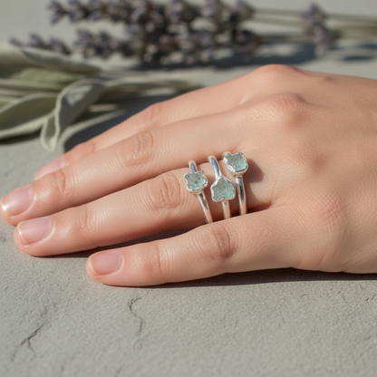 Three dainty raw aquamarine silver stacking rings worn across fingers on hand with dried botanicals